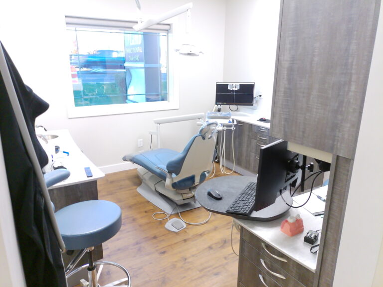 Modern treatment room with dental chair, dual monitors, and clinical equipment